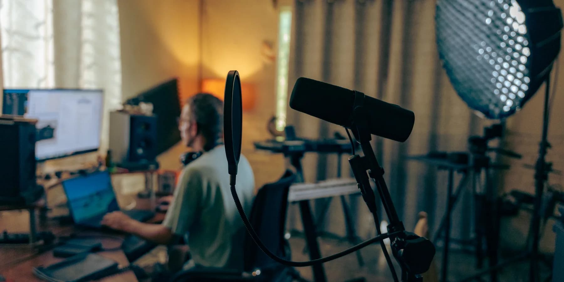 The VRTKL studio: a microphone and softbox in the foreground, someone working at a desk of monitors behind.